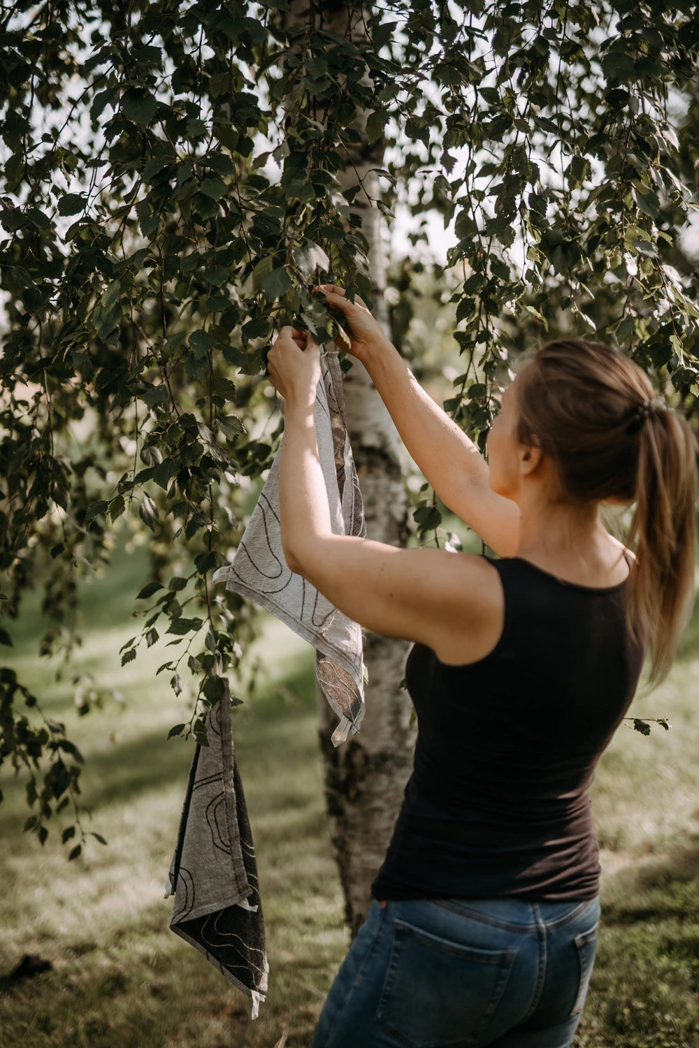 Pieni pellavapyyhe harmaa ja musta-beige kuivumassa puun oksilla